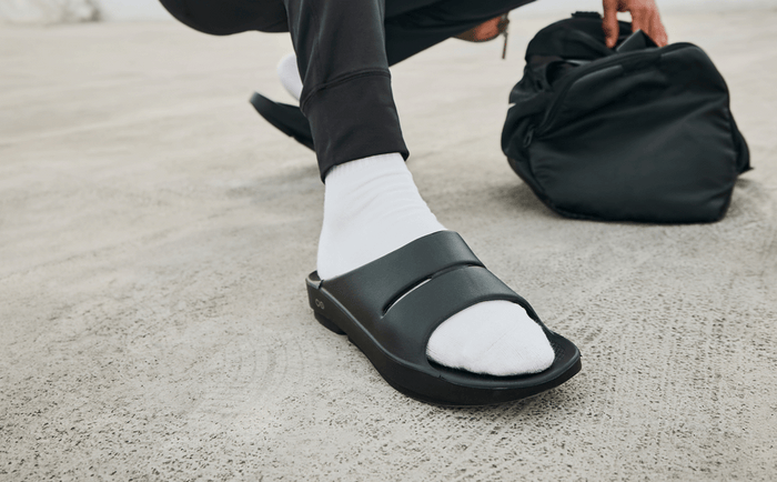 Men's OOahh Slide Sandal - Black close up of shoe on model crouching outside | lifestyle