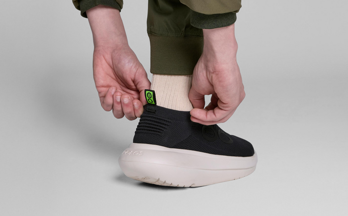 Men's OOmy Zen - Chalk Black model adjusting back of shoe in studio | lifestyle
