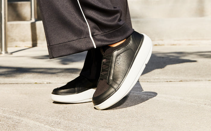 Black sneakers with white soles worn by a person on a concrete surface | lifestyle