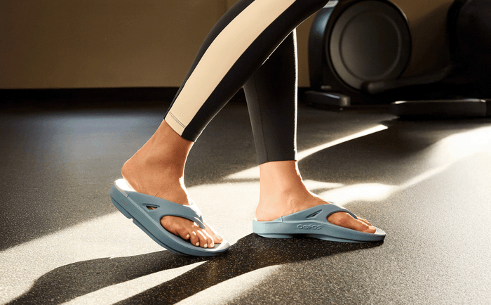 Person wearing light blue sandals on a dark floor.