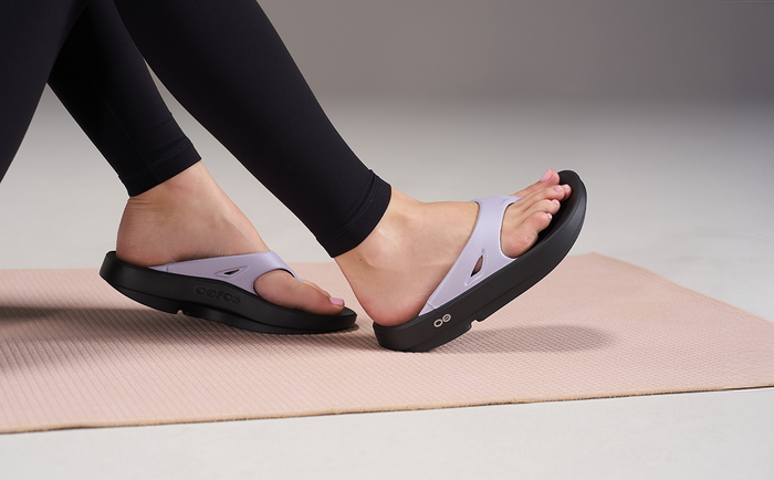 Person wearing black sandals with purple straps on a yoga mat | lifestyle